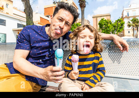 Spagna, Barcellona, felice padre e figlio seduti su un banco di lavoro godendo di un gelato Foto Stock