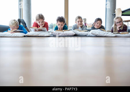 Gli alunni sdraiato sul pavimento la lettura di libri di scuola sala pausa Foto Stock