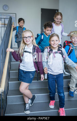 Felice gli alunni sulla scalinata che lasciano la scuola Foto Stock