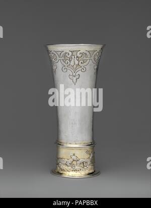 Footed becher. Cultura: Ungherese, Brassó. Dimensioni: complessivo: 7 3/16 x 3 9/16 in. (18,3 x 9 cm). Autore: eventualmente da Thomas Trepches II (master 1632, morto 1676). Data: metà del XVII secolo. La prossimità di Ungheria all'Impero Ottomano può spiegare il motivo per cui gli artigiani ungherese e patroni spesso favorito orientale-motivi di ispirazione, come il arabescati scrollwork sotto il labbro su questo bicchiere, il quale era stato fuori moda in Europa occidentale per quasi due generazioni. La scena di caccia alla base si riferisce al diritto esclusivo della nobiltà locale a caccia di alcuni animali di gioco. Letteratura Tiham Foto Stock