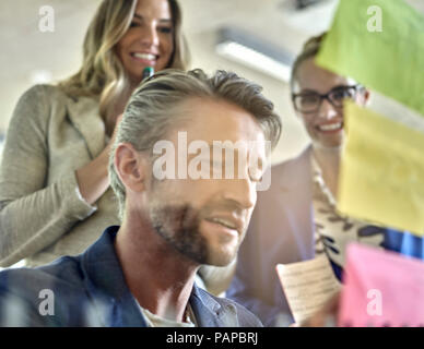 I colleghi a discutere con sticky notes al pannello in vetro Foto Stock