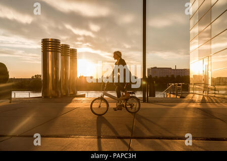 Senior di equitazione donna city bike in riva al fiume e al tramonto Foto Stock