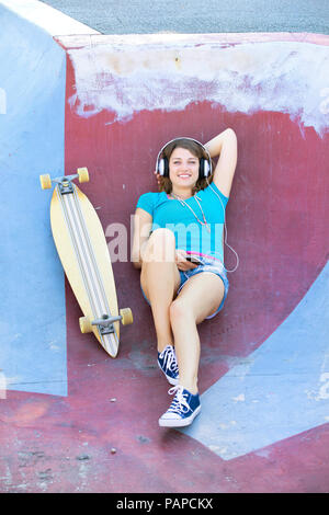 Longboarder femmina con gli auricolari che giace nella halfpipe Foto Stock