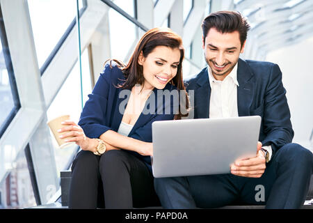Imprenditrice sorridente e imprenditore condivisione portatile su scale in ufficio moderno Foto Stock