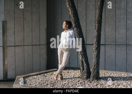 Giovane imprenditrice appoggiata contro atree in un cortile Foto Stock