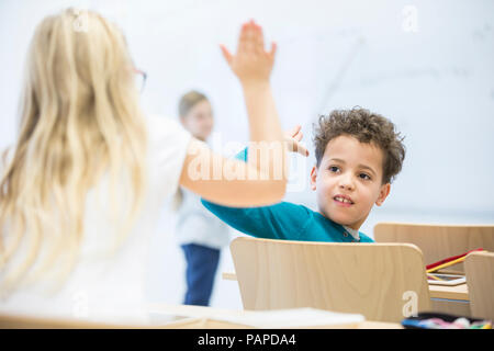 Gli alunni ad alta fiving in classe Foto Stock