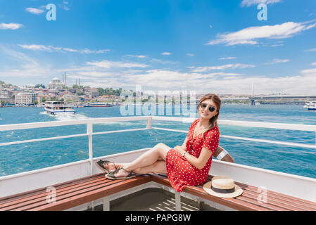 Bella donna in abito rosso si siede su un traghetto con vista del paesaggio di Istanbul il background. Foto Stock