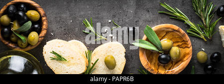 Olive nere e verdi olio d'oliva e pane nero su sfondo di ardesia. Lunga formato banner. Foto Stock