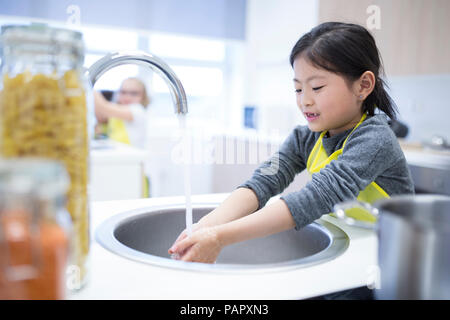 Schoolgirl lavando le mani nel corso di cucina Foto Stock