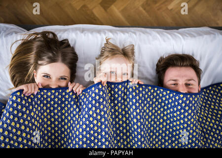 La famiglia felice giacente in letto, nascondendosi sotto coperta Foto Stock