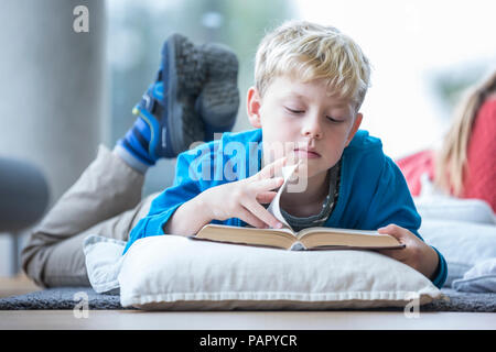 Scolaro sdraiato sul pavimento la lettura di libri di scuola in sala pausa Foto Stock