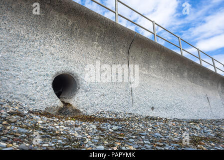 Una tempesta di uscita di scarico impostato in concreto la parete del mare su una spiaggia di ciottoli a Criccieth, Galles. Foto Stock