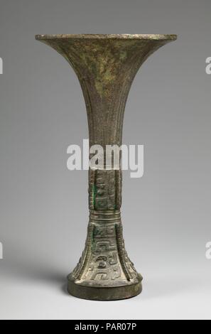 Rituale del bicchiere di vino (GU). Cultura: la Cina. Dimensioni: H. 12 a. (30,5 cm); Diam. di RIM: 3 1/2 in. (8,9 cm); Diam. di base: 6 1/2 in. (16,5 cm). Data: ca. Il XIII secolo A.C. Questo, alta e slanciata, bicchiere di vino ha un profilo drammatico che le curve in una ininterrotta arco da rim a piedi. Tre registri orizzontali di decorazione, separate da bande strette di linee in rilievo, creare un piano articolato. Il registro superiore è costituito da quattro lame rastremate di ornamento che sottolineano la graziosa curva verso l'alto della svasatura collo. Il medio e registri di fondo sono costituiti da grassetto maschere taotie sollevato su un polv Foto Stock