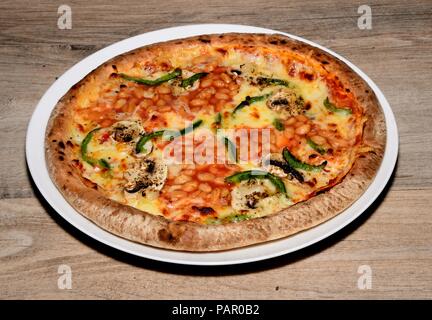 Tutta la pizza tonda e rabboccato con formaggio, pomodoro, peperoni verdi, i funghi e i fagioli, England, Regno Unito, Europa. Foto Stock