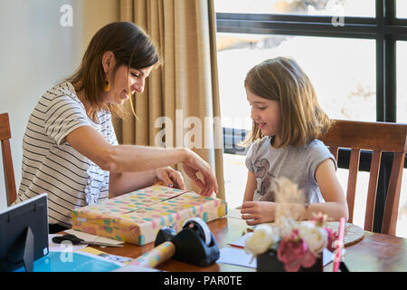 Madre e figlia dono di imballaggio a tavola in casa Foto Stock