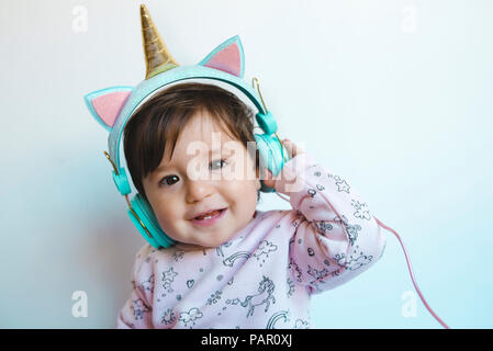 Ritratto di sorridente bambina con cuffie unicorn ascoltando musica Foto Stock