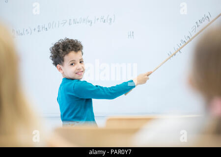 Scolaro spiegando formula a lavagna in classe Foto Stock