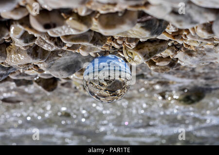 Palla di vetro seduto alla spiaggia rocciosa whit mare onda riflessa in esso/ immagine concettuale delle vacanze estive Foto Stock