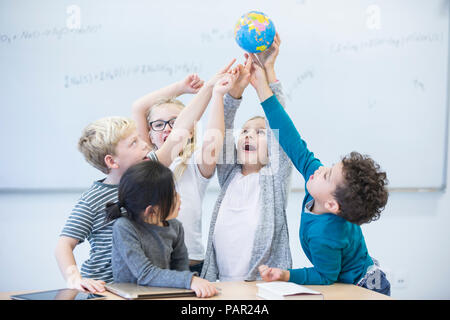 Felice gli alunni holding globe insieme in classe Foto Stock