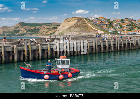 Una piccola barca da pesca lascia il pittoresco porto di West Bay nel Dorset, reso famoso come il luogo per la serie televisiva "Broadchurch'. Foto Stock