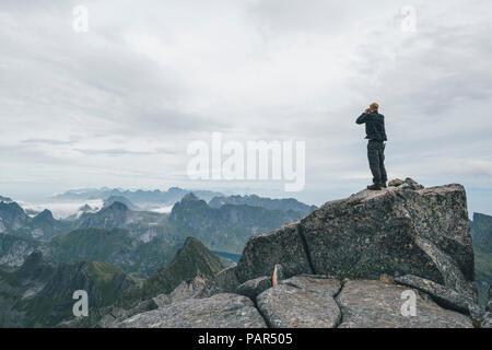 Norvegia Lofoten, Moskenesoy, giovane uomo in piedi alla Hermannsdalstinden, guardando sopra Kjerkefjord Foto Stock