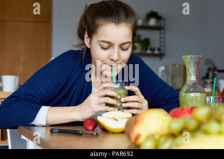 Ragazza seduta in cucina, casalinga potabile frullato di frutta Foto Stock