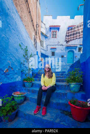 Giovane donna siede su scale nella città vecchia, blue house facciate, medina di Chefchaouen, Chaouen, Tangier-Tétouan, Marocco Foto Stock