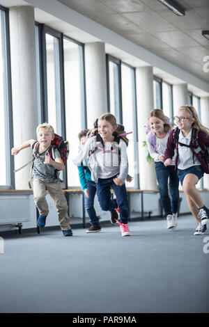 Emozionato alunni correre verso il basso corridoio della scuola Foto Stock