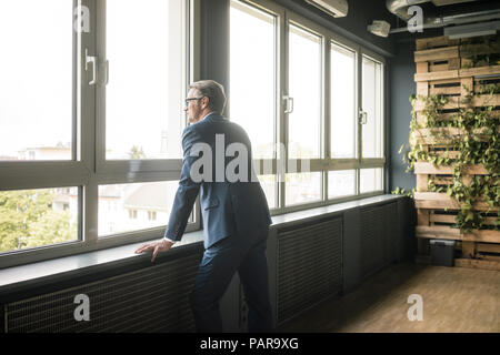 Imprenditore maturo in piedi presso la finestra di office Foto Stock