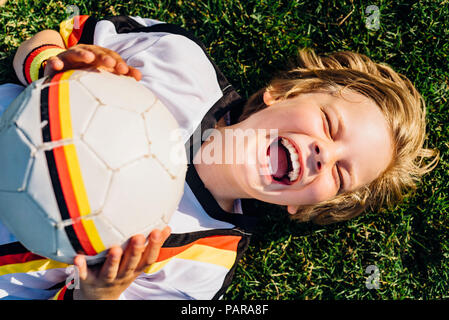 Ragazzo in calcio tedesco shirt giacente su erba, ridevano allegramente Foto Stock