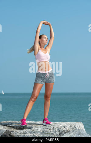 Montare sportivo da donna stretching le sue braccia, il riscaldamento esercizi al di fuori del mare Foto Stock