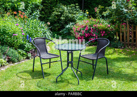 Tavolo e sedie nel giardino pieno di fiori d'estate Foto Stock