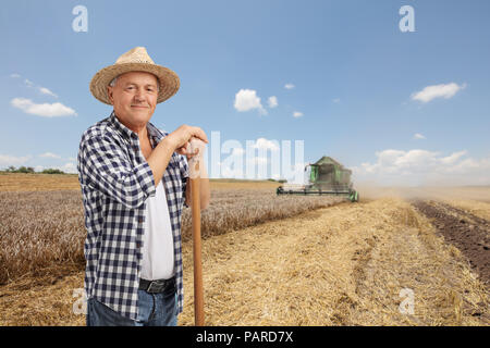 Anziano contadino su un campo di grano con una mietitrebbia Foto Stock