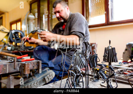 Scultore è rendere le figure creative di musicisti di filo metallico nella sua bottega. Fisarmonicisti suonano insieme. Foto Stock