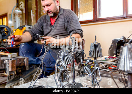 Scultore è rendere le figure creative di musicisti di filo metallico nella sua bottega. Fisarmonicisti suonano insieme. Foto Stock