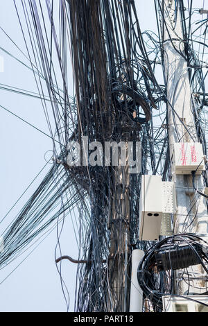 Un groviglio di cavi disordinato su un palo stradale a Phnom Penh, Cambogia, che rappresenta lo sviluppo urbano disorganizzato e la crescita tecnologica Foto Stock