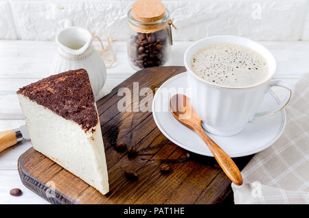 Tazza di caffè con torta al formaggio o formaggio morbido nel caffè sul vecchio bianco sullo sfondo di legno, vista dall'alto, copia spase Foto Stock
