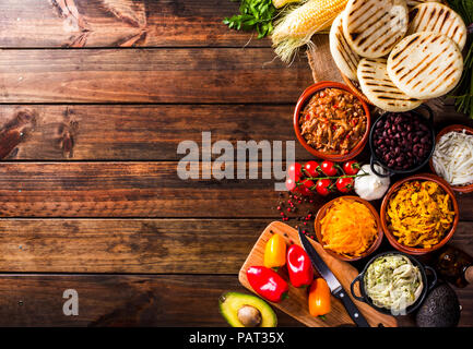 Vista da sopra del legno di un tavolo rustico con svariati ingredienti per la cottura e il riempimento arepas, tipico cibo latino-americano. Tutti gli ingredienti sono Foto Stock