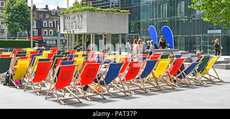 Le persone che si godono la seduta in estate sole sdraio colorate al di fuori del blocco di ufficio vicino a coffee & food bar appena prima di ora di pranzo Londra Inghilterra REGNO UNITO Foto Stock