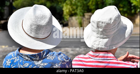 Senior donna matura seduta in attesa presso la fermata su molto caldo 2018 ondata di caldo giorno d'estate indossa cappello bianco nel sole di mezzogiorno Haworth West Yorkshire England Regno Unito Foto Stock