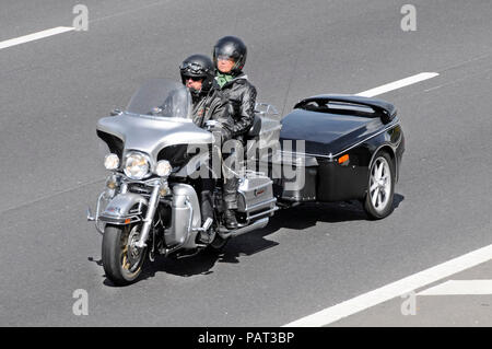 Maschio di motociclista indossando un microfono & donna in sella moto passeggero pillion giovane che indossa un casco insolita di traino rimorchio in autostrada del Regno Unito Foto Stock