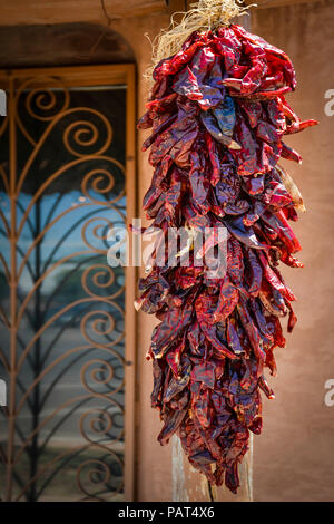 Un appeso srand del rosso essiccato chii pepi noto come Ristras, tradizionalmente utilizzate in New Mexican cusinie appendere da una vecchia dimora di adobe in NM Foto Stock