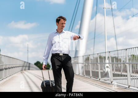 Imprenditore con valigia scorrevole su un ponte controllando il tempo Foto Stock