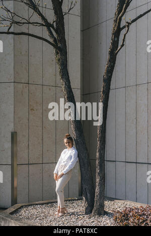 Giovane imprenditrice appoggiata contro atree in un cortile Foto Stock