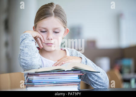 La scolaretta leggendo un libro sul tavolo a scuola Foto Stock