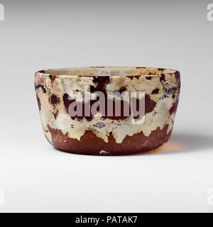 Vaso di vetro. Cultura: Romano. Dimensioni: H.: 2 3/8 in. (6 cm) Diam.: 4 3/8 in. (11,1 cm). Data: fine del I secolo A.C. - inizio del I secolo d.c. Miele traslucido marrone. Arrotondato bordo verticale; leggermente rigonfia i lati rastremandosi verso il basso; il fondo piatto. Ruota orizzontale-taglio delle scanalature sulla parte interna; singola scanalatura 1,05 cm al di sotto di RIM, banda di due scanalature 3.35 cm al di sotto di RIM. Completa, tranne per il piccolo chip nel cerchio; rotti e riparati intorno ad un lato del cerchio; molto poche bolle; assopimento e vaiolatura, patch di iridescenza e spessi e di resistenza agli agenti atmosferici di consistenza cremosa. Rettifica circolare contrassegni sulla parte interna del fondo. Museo: Metropol Foto Stock