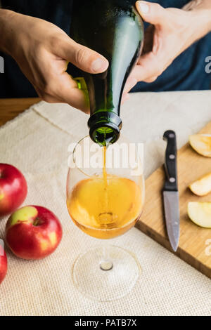 Vista superiore dell'uomo premium versatore cidre in vetro. Close-up di mani maschio versando vintage vino di mele in bella in vetro tavolo rustico sfondo con Foto Stock