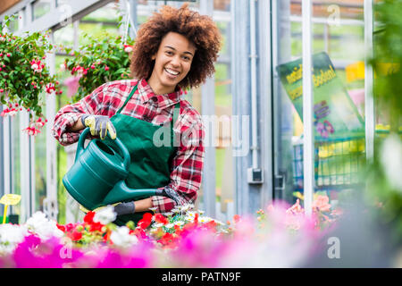 Bella giovane donna abbeveraggio vari vasi houseplants per la vendita Foto Stock