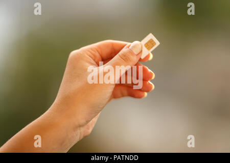 Mano femmina bianco di contenimento della scheda SIM su sfondo blured Foto Stock