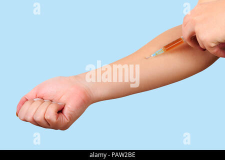 Close-up di mano, dando la vaccinazione per paziente utilizzando una siringa con farmaci marrone. Iniezione sterile nel braccio su fondo azzurro. tossicodipendente Foto Stock